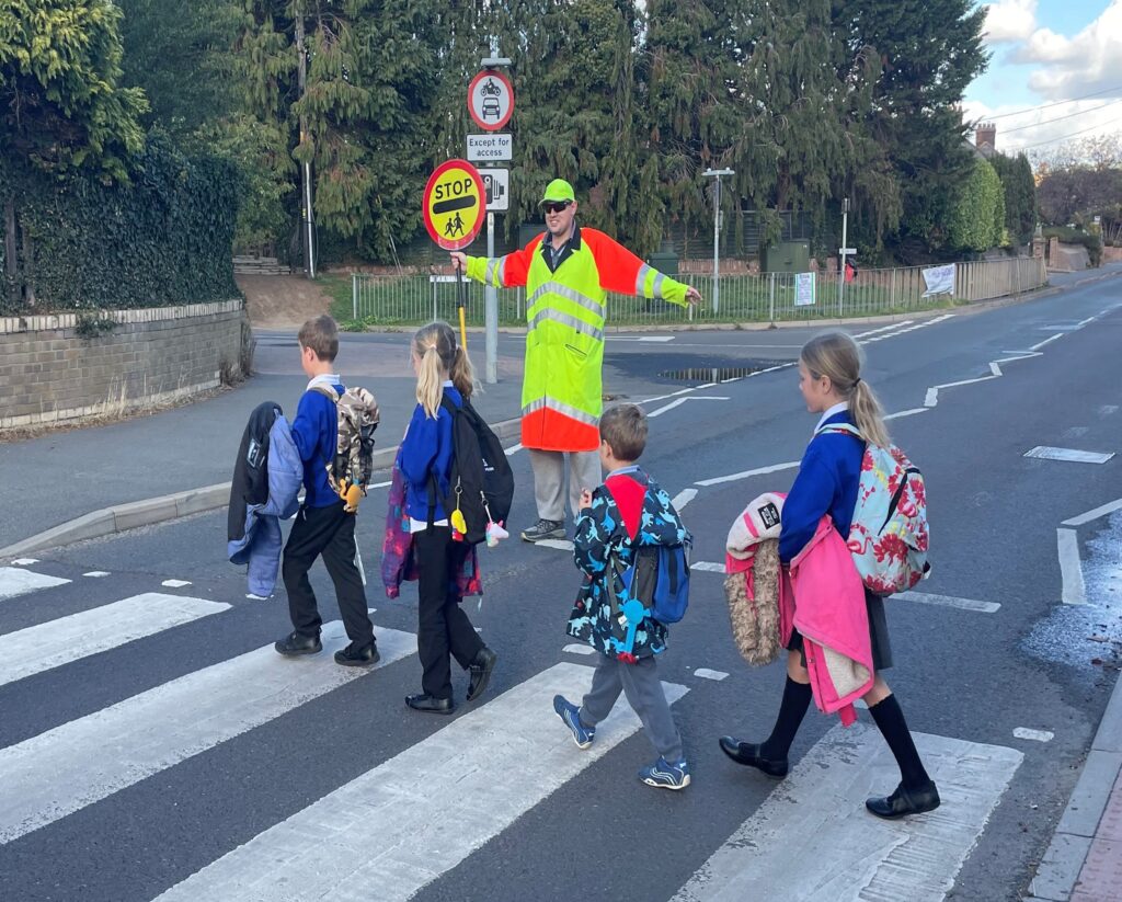 children crossing on a zebra crossing helped by a school crossing patrol